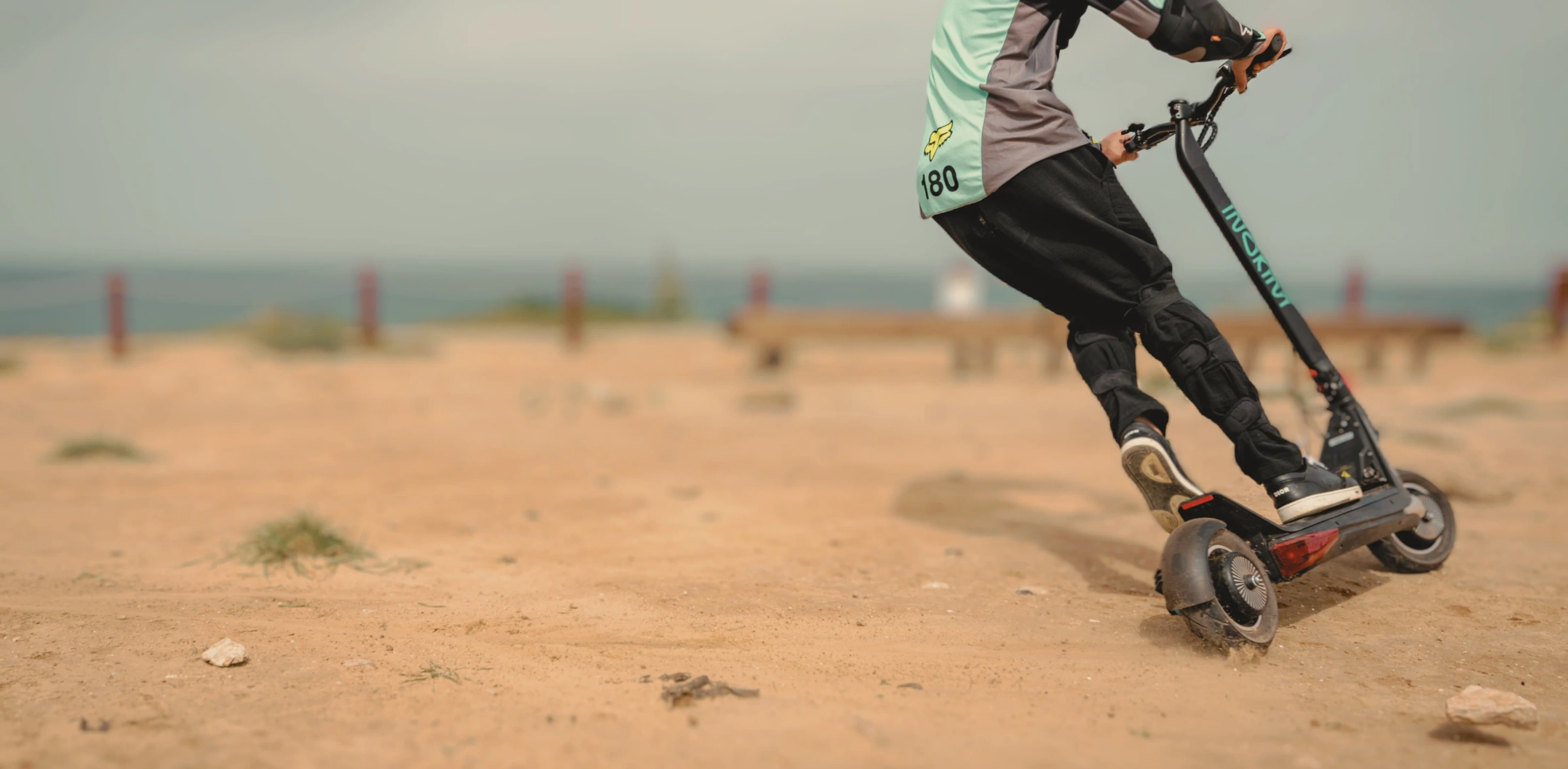 Rider in a mint jersey leaning an Inokim scooter through a turn on sandy ground