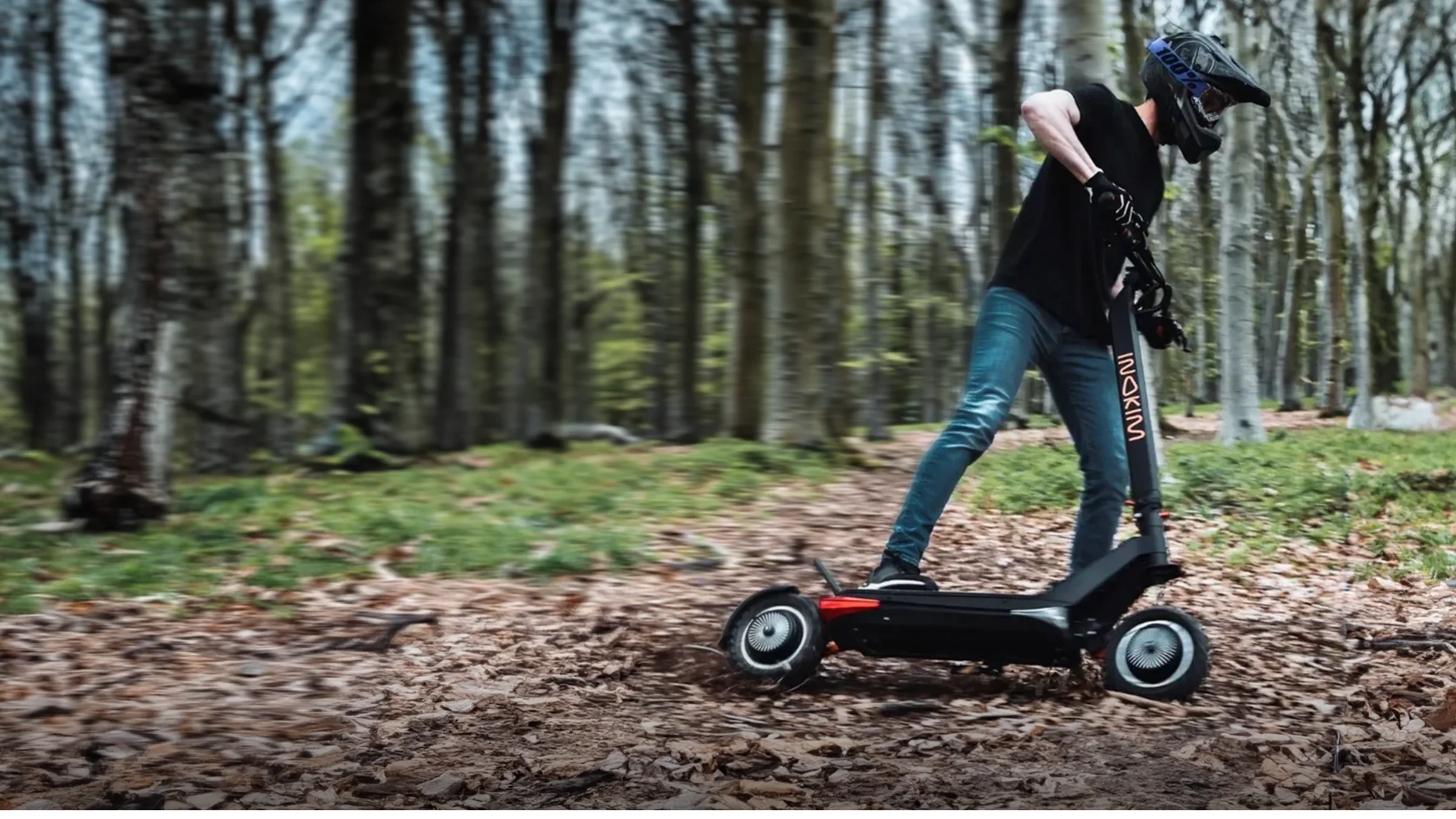 Rider in a full-face helmet cornering an Inokim scooter on a leafy forest trail